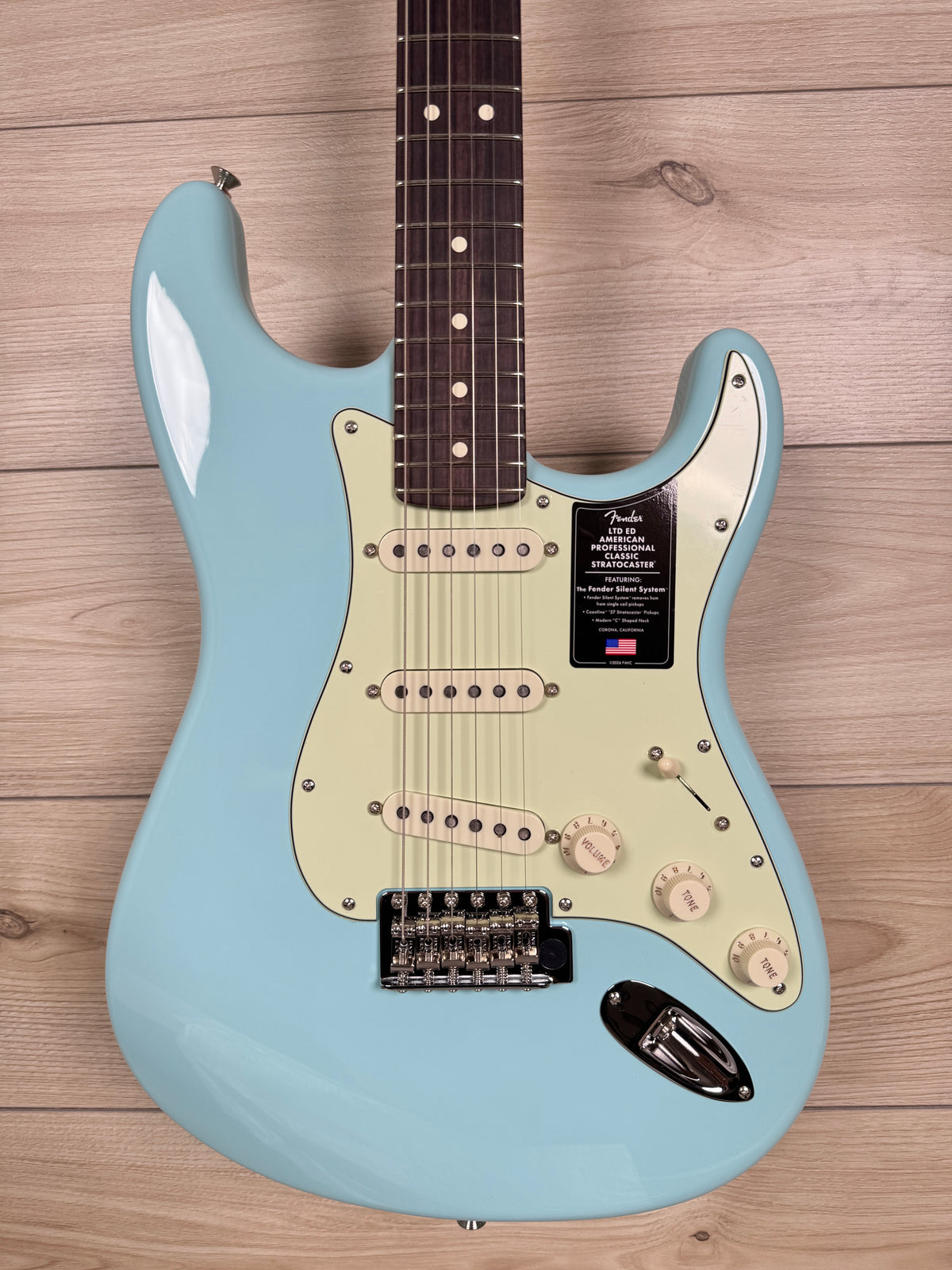 A Fender Stratocaster American electric guitar in light blue with a cream pickguard, laid flat on a light wood plank background.