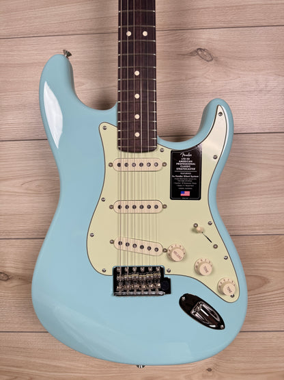 A Fender Stratocaster American electric guitar in light blue with a cream pickguard, laid flat on a light wood plank background.
