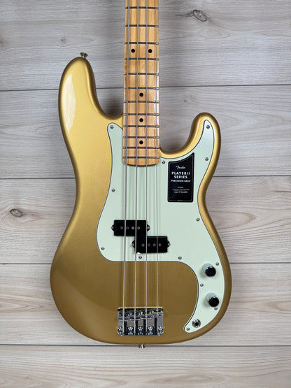A gold-finish Fender Stratocaster electric bass guitar with a cream pickguard and maple neck, photographed from the front against a light gray wood plank background.