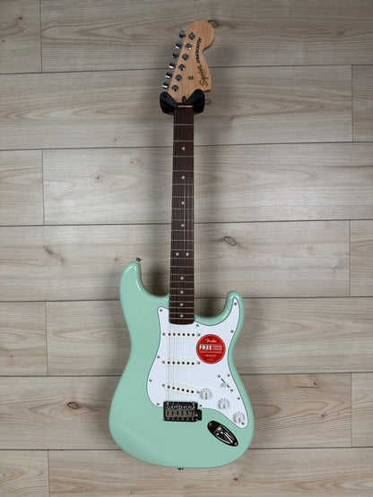 A Squier electric guitar with a white pickguard in surf green finish
