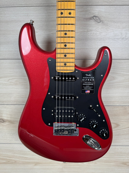 A Fender American Ultra electric guitar in metallic red with a black pickguard and maple fretboard, photographed from the front against a light wood plank background.