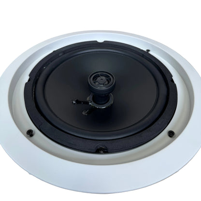 A ceiling-mounted recessed speaker with a black driver and a white circular frame, shown from a top-down perspective on a light wood floor.