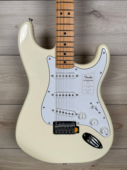 A Fender Stratocaster electric guitar in cream with a maple neck, photographed from a top-down angle on a light wood plank background.
